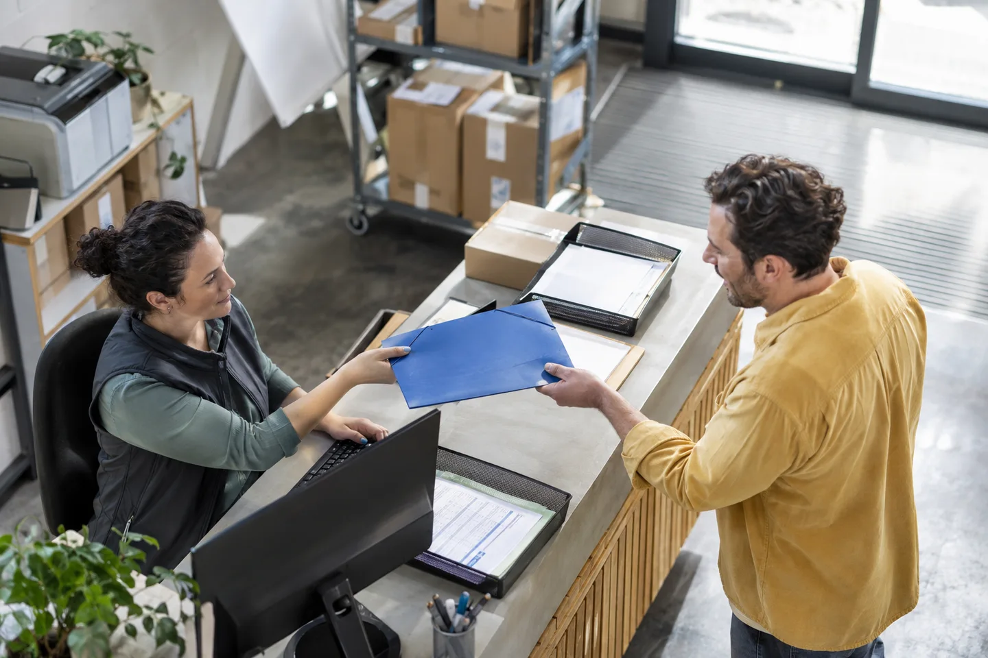 A coordinator handing a blue request folder to its receiving colleague